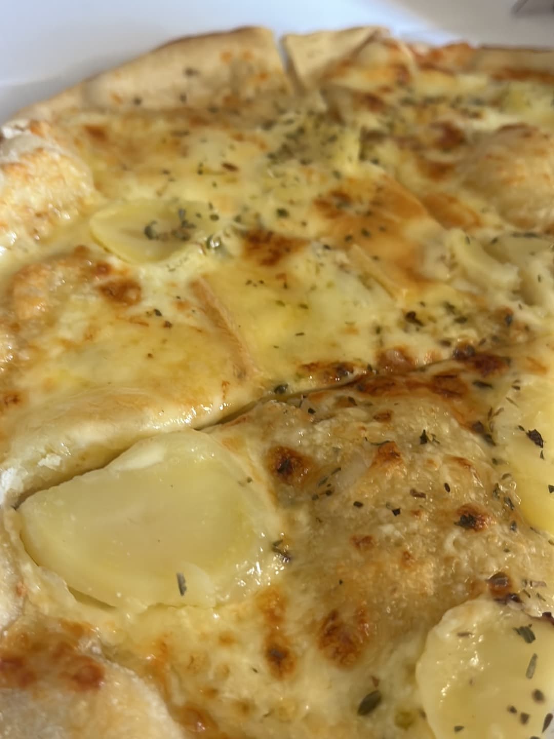 Gros plan sur une pizza à base de crème fraîche, rondelles de pomme de terre, fromage doré et origan, avec sa croûte gonflée