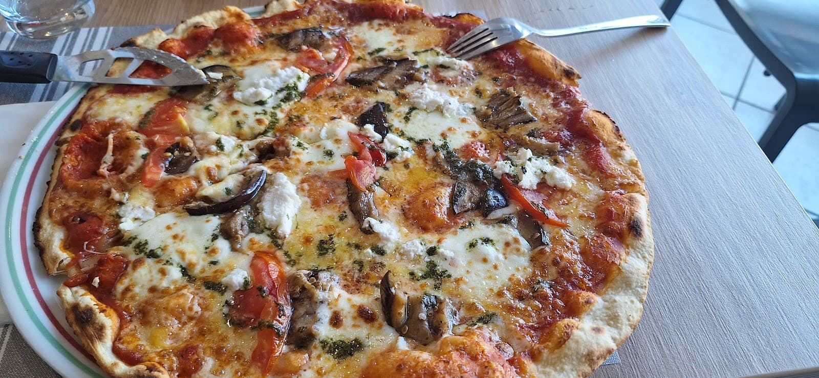 Pizza garnie de mozzarella fondue, de ricotta, d’aubergines, de tomates fraîches et de basilic, servie sur une assiette à table
