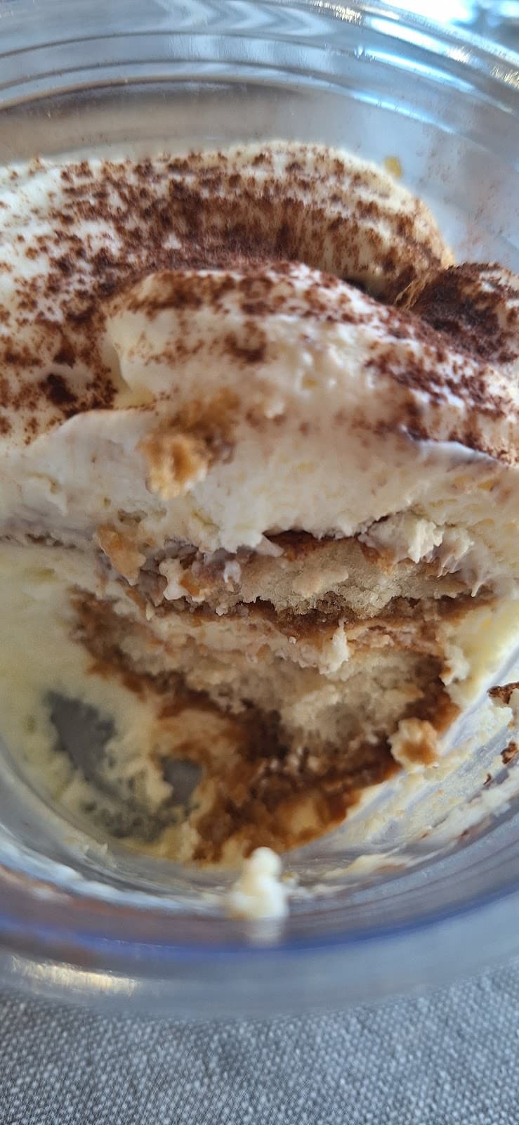 Très gros plan dans un pot de tiramisu : crème au mascarpone saupoudrée de cacao et couches de biscuits imbibés de café