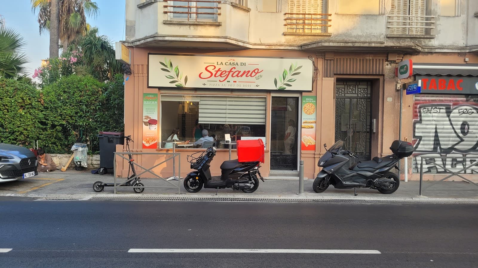 La devanture de La Casa di Stefano avenue de la Liberté : enseigne rouge et blanche « Pizza au feu de bois », vitrine ouverte sur la salle et scooters de livraison garés devant